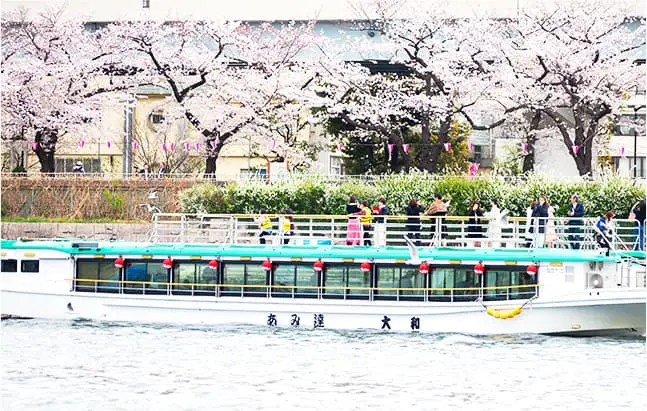 隅田川で屋形船からお花見をする人々